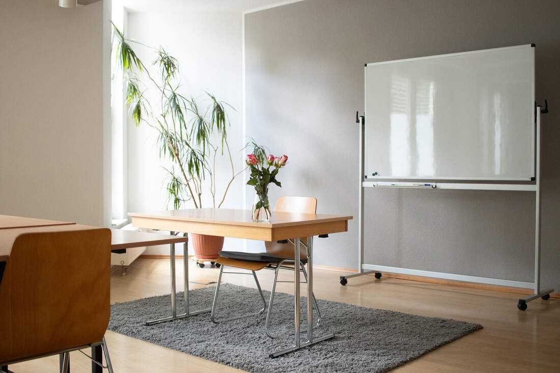 Seminarraum 1: Tisch mit Stühlen, Grünpflanze und mobilem Whiteboard